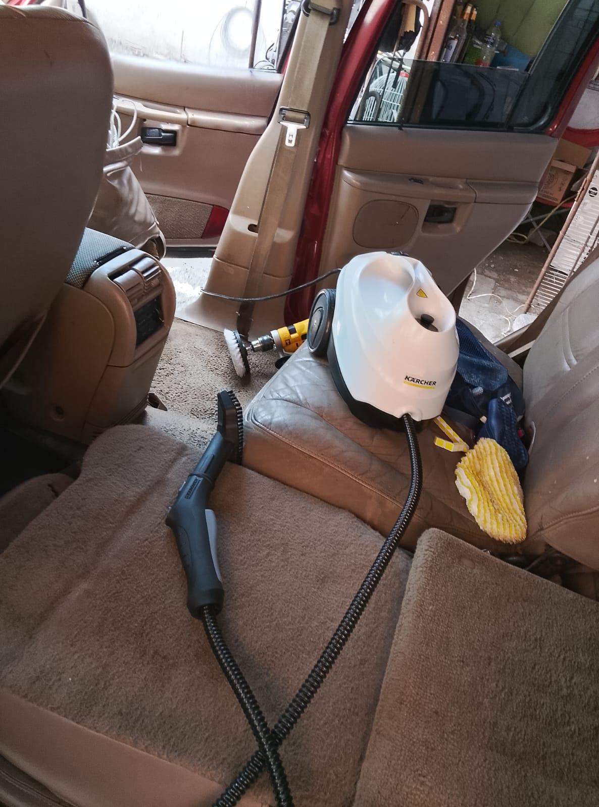 Interior de un vehículo con equipo de limpieza sobre el asiento trasero.